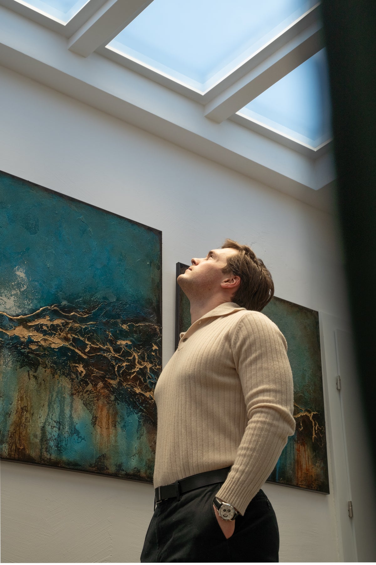 Mężczyzna w galerii z odchyloną do tyłu głową, patrzący w górę na świetliki nad sobą